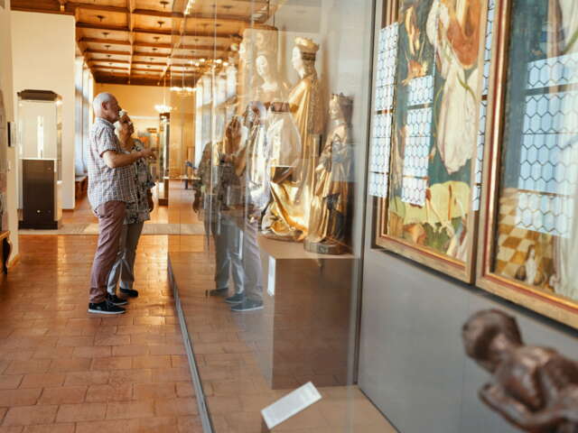 Zwei Besucher die sich die Ausstellung im Museum zu Allerheiligen anschauen. In den Schaukästen sind alte Kirchenfiguren.